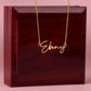 Signature name necklace with "Ebony" in gold finish on mahogany box background.